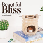 Marble oil burner with a lit candle on books, surrounded by a cactus and decorative stones, with 'Beautiful Bliss' text.