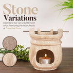 Stone-patterned oil burner with a lit candle on a wooden surface, surrounded by greenery.