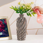 Person watering a vase with flowers on a table next to a framed picture.