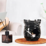 Black marble-patterned wax warmer with a candle on a woven coaster, next to a black reed diffuser.